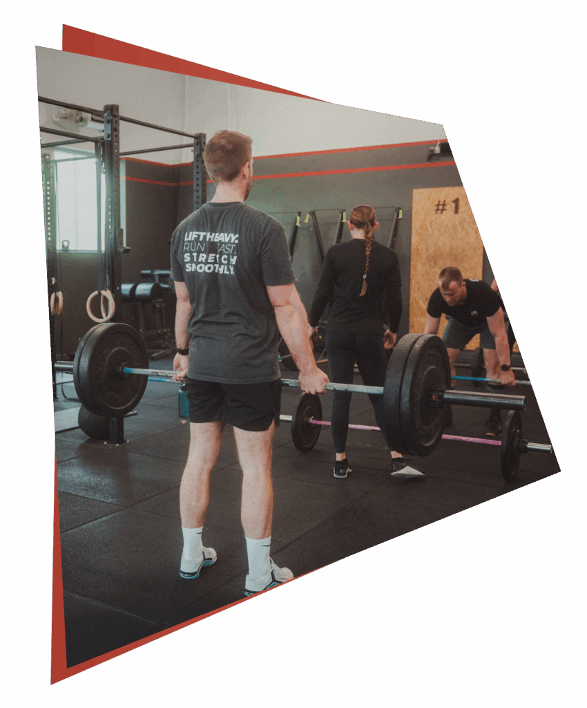 Drei Personen trainieren in einem Fitnessstudio, um ihre Fähigkeiten zu verbessern. Ein Mann im Vordergrund hebt eine Langhantel, während zwei andere im Hintergrund Gewichte vorbereiten und sich dehnen. Das Fitnessstudio bietet verschiedene Fitnessgeräte und Kurse an, um Kraft und Technik zu verbessern.